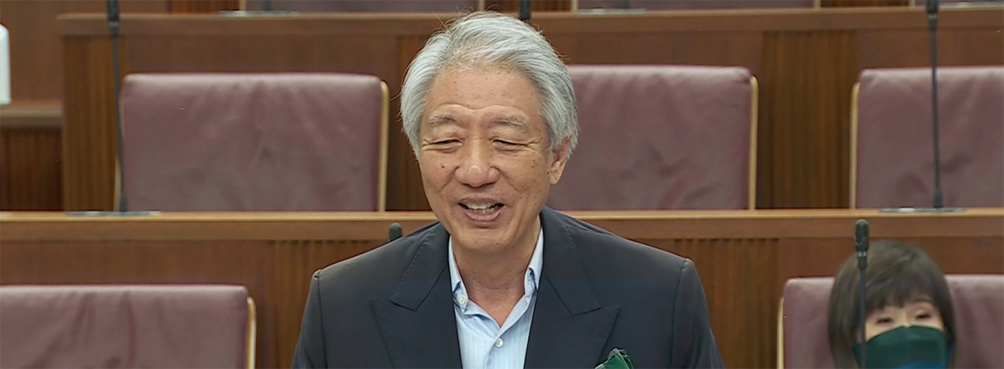 Man with gray hair, smiling, in suit, seated in a room with brown leather seats.